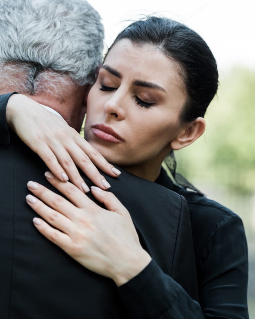 upset woman with closed eyes hugging senior man